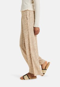 Pantaloni a gamba larga con motivo tannato e design floreale, dotati di una cintura elastica. Abbinati a sandali flat con dettagli intrecciati.