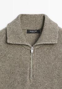 Pull en tricot gris avec un col zippé à mi-hauteur, tissu texturé et une étiquette indiquant "Massimo Dutti". Quincaillerie de la fermeture éclair au niveau du col.