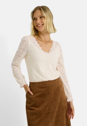 Haut en dentelle à manches longues en blanc cassé avec un col festonné et un motif texturé, associé à une jupe en daim brun avec des poches.