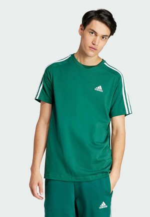 Camiseta de algodón verde con mangas cortas, tres franjas blancas en los hombros, cuello redondo y logo blanco de Adidas en el pecho.