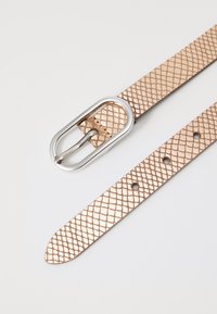 Ceinture en faux cuir métallisé rose avec un motif de diamant texturé et une boucle ovale en argent. Comprend plusieurs encoches pour ajustement.