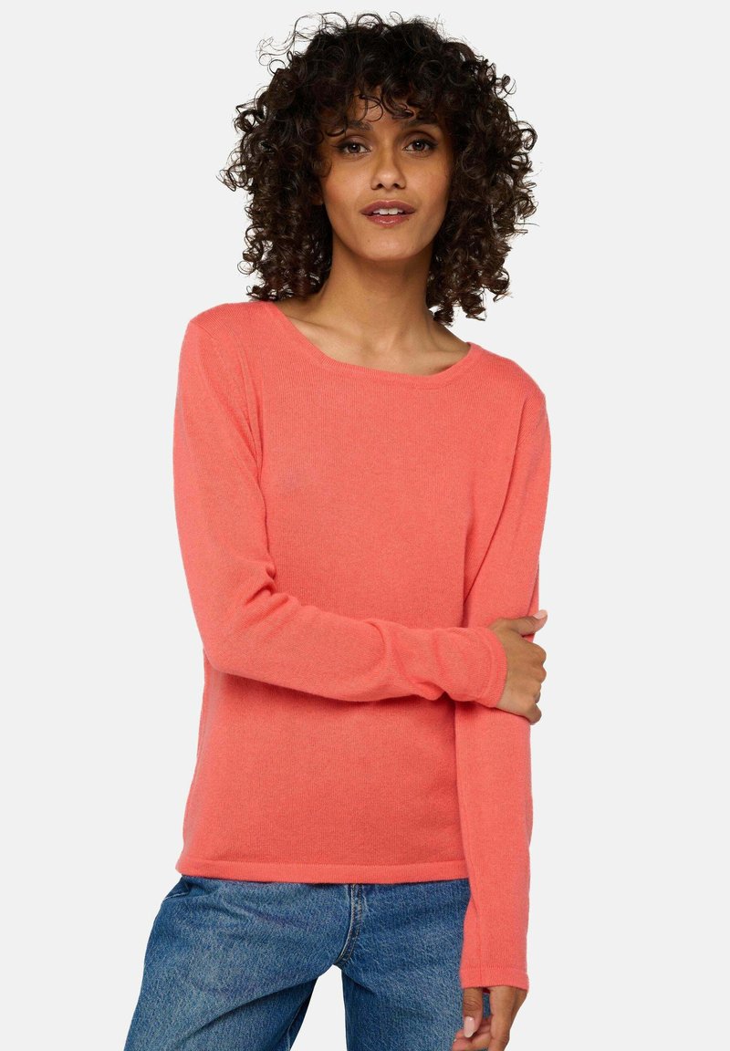 Pull-over à manches longues corail avec une texture douce, un col rond et des manches ajustées, associé à un jean bleu.