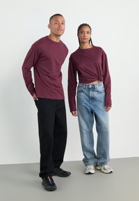 Mørkerøde langermede skjorter på to personer, kombinert med svarte bukser og lyseblå jeans. Begge bruker sneakers; den ene skjorten er knyttet i livet.