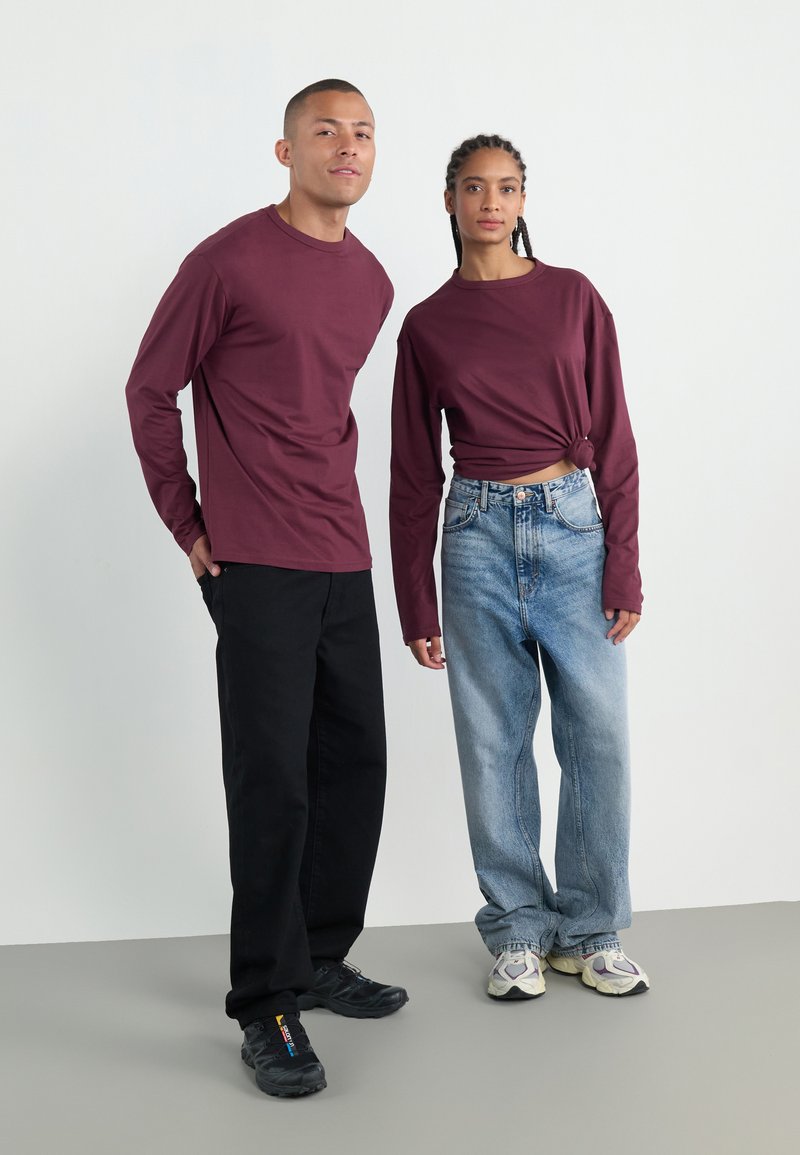 Mørkerøde langermede skjorter på to personer, kombinert med svarte bukser og lyseblå jeans. Begge bruker sneakers; den ene skjorten er knyttet i livet.