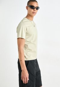 T-shirt vert clair à manches courtes en coton doux avec un col rond, associé à un short noir et des lunettes de soleil noires en forme de chat.