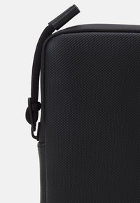 Borsa nera con zip, con una superficie testurizzata, angoli arrotondati e una maniglia robusta. Presenta una zip liscia e un'etichetta elastica.
