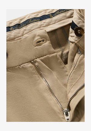 Beige Hosen aus glattem Stoff, mit einem Messingsreißverschluss, Knopfverschluss und einem blauen Etikett mit goldenem Text "Brooks Brothers" darin.