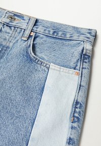 Jean en denim bleu clair avec un effet dégradé, des accessoires en cuivre, un design classique à cinq poches et un détail de color-blocking distinct.