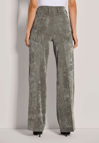 Hochtaillierte, weit geschnittene Hosen aus gedämpftem grünen Baumwollcord. Sie verfügen über vertikale Rippungen, zwei Gesäßtaschen und eine weiche, strukturierte Oberfläche.