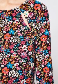 Floral-patterned dress featuring a black background with multicolored flowers. Notable design includes a shoulder cut-out detail.