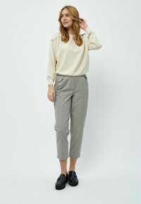 Top color crema a maniche lunghe con vestibilità comoda; pantaloni cropped a righe grigie con bottoni decorativi; mocassini neri completano l'outfit.