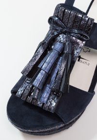 Sandale en daim bleu marine avec des pampilles en cuir texturé et brillant, un nœud sur la bride avant et une semelle plateforme tressée.