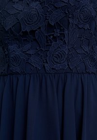 Robe navy avec un corsage en dentelle florale à broderies en relief, complétée par une jupe en tissu uni fluide.