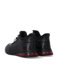 Schwarze Sportschuhe mit einem glatten Ledereinsatz, gepolstertem Kragen, roten Akzenten und einer strukturierten Gummisohle mit Sichtkissen.
