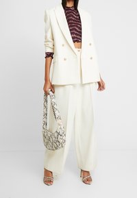 Dubbelknäppt vit blazer över en mörk mönstrad crop top, kombinerad med vida byxor och en hobo-väska i ormtryck. Klackar med remmar.