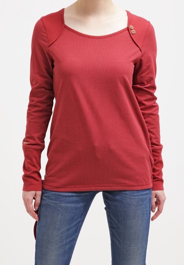 Långärmad röd topp med textilstruktur, rund halsringning och tre träknappar på vänster axel. Kombination med blå jeans.