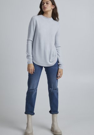 Light blue knitted sweater with a crew neckline, paired with distressed blue jeans and beige ankle boots. Smooth texture and relaxed fit.