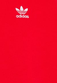 Camiseta de algodón roja con un pequeño logo blanco de Adidas en la parte superior izquierda. La tela tiene una textura suave, garantizando comodidad.