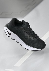 Black athletic shoe featuring a textured upper, woven pattern, black laces, and a white sole with a wave-like design. Nike logo on side.