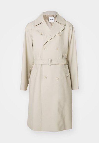 Trench coat beige doppiopetto con cintura. Presenta ampi rever, tasche laterali e un tessuto morbido e strutturato.
