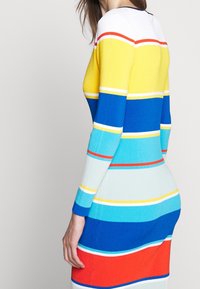 Abito lavorato a maglia con strisce orizzontali in giallo, blu, turchese e rosso. Design aderente con texture a coste e maniche lunghe. Collo rotondo.