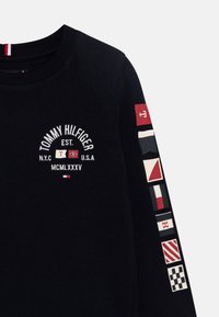 T-shirt nero a maniche lunghe in cotone, con un design del logo circolare e motivi di bandiere nautiche sulla manica destra.