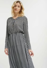 Abito a maniche lunghe in motivo pied de poule bianco e nero, caratterizzato da un collo con coulisse e una vita elastica per un fit comodo.