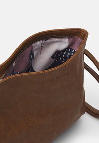 Brązowa skórzana torba z zamkiem błyskawicznym, z podszewką w kolorze fioletowym i granatowym, ozdobioną kropkami i abstrakcyjnymi wzorami.