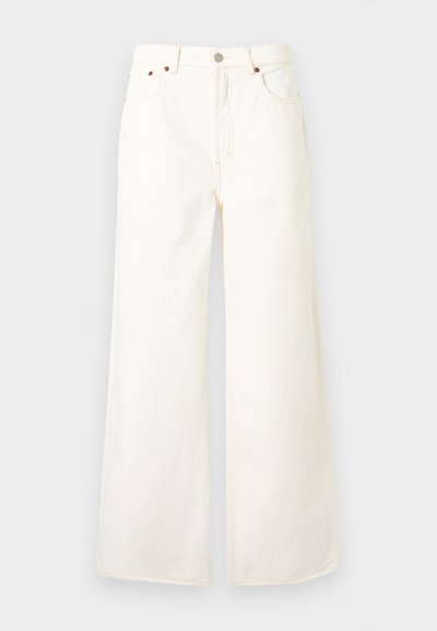 Kõrge vöökohaga valged laiade säärtega teksad, millel ees nupud ja tõmblukk, viie taskuga disain ning vaskne nupukinnitused.