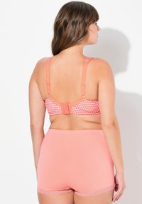 Rosa gepunkteter BH mit verstellbaren Trägern und Hakenverschluss, kombiniert mit passenden rosa Boyshorts, die einen Spitzenbesatz an den Rändern haben.