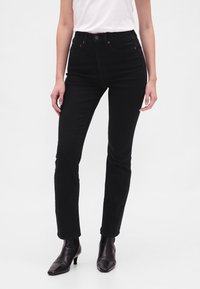 Črne jeans hlače z visokim pasom v ozkem kroju, izdelane iz jeansa. Vsebujejo pet žepov, sprednjo zapenjavo na gumbe in subtilne šive.