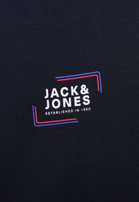 Camiseta de algodón azul marino con un logo blanco "JACK & JONES" con acentos en rojo y azul, junto con "ESTABLISHED IN 1990" debajo del logo.