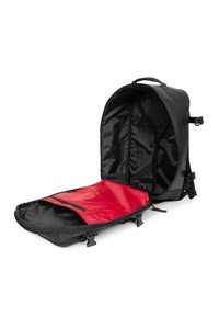 Mochila negra con un diseño curvado. Presenta un forro interior rojo y correas ajustables. Cierre de cremallera con herrajes externos de plástico.