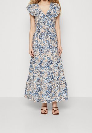 Robe maxi à motif floral bleu et beige, avec des manches volantées, un décolleté en V et une jupe à volants. Sandales brunes à lanières.