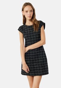 Mustavalkoinen ruudullinen mekko lyhyillä hihoilla, teksturoidusta kankaasta, tiukasti istuva siluetti, päättyen polven yläpuolelle.