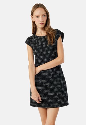 Robe à carreaux noir et blanc avec des manches courtes, en tissu texturé, et une silhouette ajustée, se terminant au-dessus du genou.