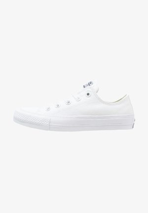 Zapatilla baja de lona blanca con suela de goma blanca, con cordones en la parte delantera y un sutil logotipo en la lengüeta y el talón.
