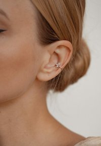 Orecchino a cuffia in argento con un delicato design a foglia adornato con piccoli cristalli, posizionato sul lobo dell'orecchio su uno sfondo chiaro.