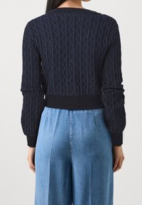 Marineblauer, kurz geschnittener Strickpullover mit Rippbündchen an Ärmeln und Saum; getragen über hellblauen, weitem Jeanshosen. Durchgehend strukturierte Details.