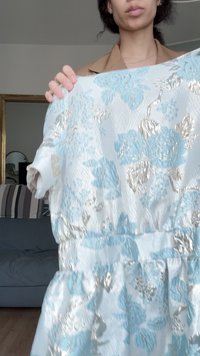 Ανοιχτό μπλε φόρεμα με ασημένια λουλουδάτα σχέδια, φτιαγμένο από υφή ύφασμα. Διαθέτει κοντά μανίκια και συγκεντρωμένη μέση για έναν συμπαγή σχήμα.