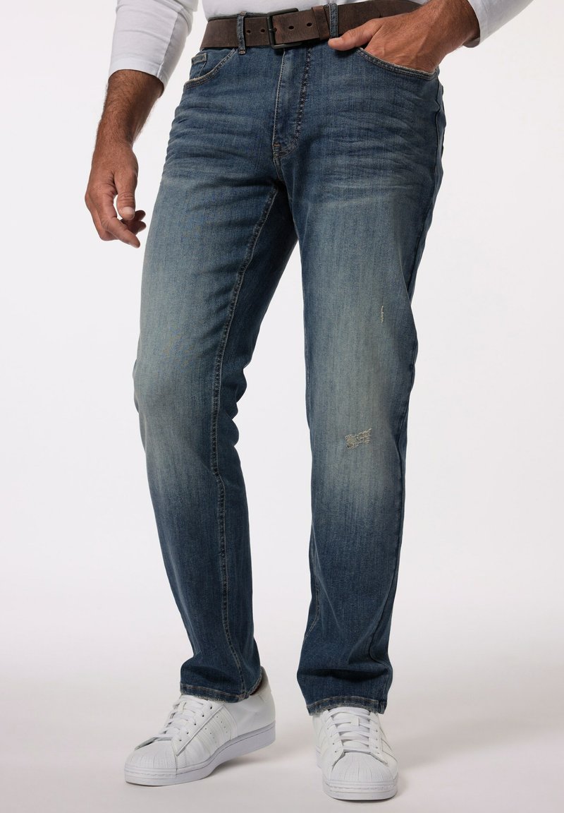 Jeans de mezclilla azul para hombre con un diseño desgastado, ligeras zonas de desgaste y un corte recto. Combinados con zapatillas blancas y un cinturón marrón.