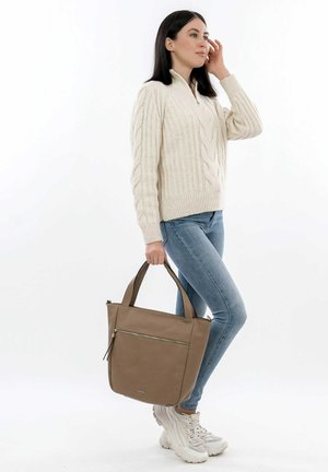 Sac fourre-tout marron avec deux poignées, texture lisse, poche zippée à l'avant, assorti à un pull crème en tricot torsadé et à un jean bleu clair.