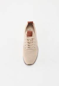 Beige strikket sneaker med en struktureret overdel, rund tå, snørebånd foran og brun læderdetalje på hælen og tunge.
