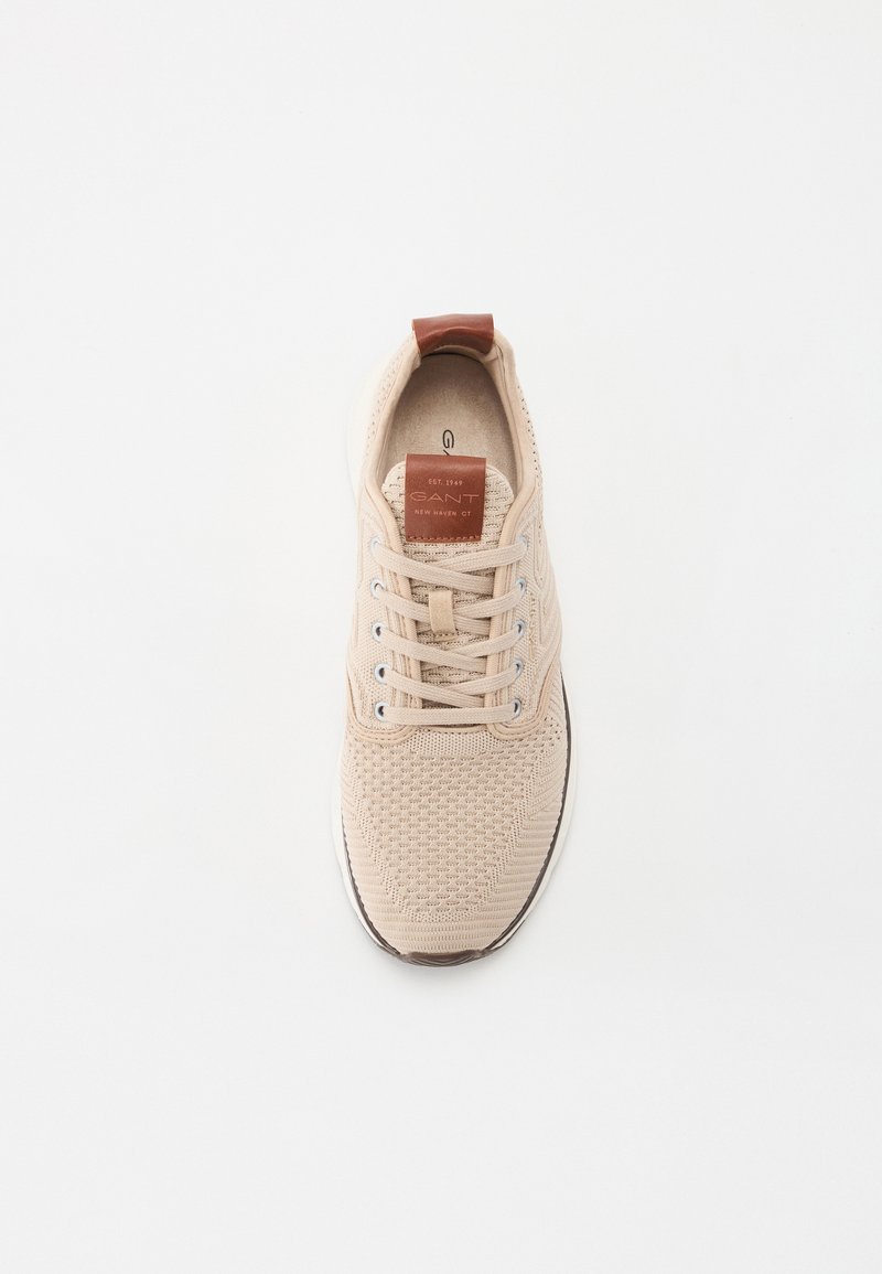 Baskets tricotées beiges avec une tige texturée, bout rond, fermeture à lacets à l'avant, et accent en cuir marron au talon et à la languette.