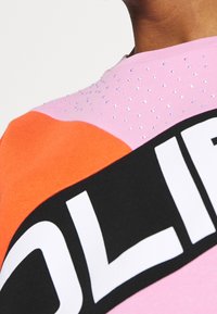 Sudadera colorida con paneles en rosa, naranja y negro. Adornada con pequeños strass y un logo blanco en negrita. Textura de tela suave.