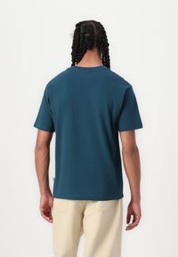 Kortærmet teal t-shirt lavet af bomuld med rund halsudskæring. Minimalistisk design, ensfarvet og med et lille mærke i sidefoden.