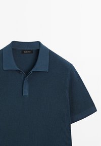 Polo shirt blu scuro con un motivo a maglia testurizzata, maniche corte e colletto piatto con chiusura a bottoni. Etichetta del brand visibile.