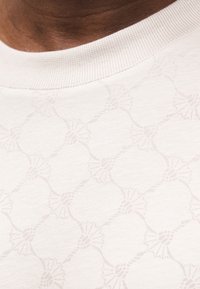 Φόρμα σε ανοιχτό μπεζ χρώμα με υφασμάτινο λουλουδάτο σχέδιο, στρογγυλή ριμπ λαιμόκοψη και λεία επιφάνεια υφάσματος. Διακριτική λεπτομέρεια στο σχέδιο εμφανής.