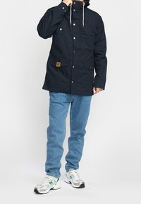 Mörkblå huvjacka med tryckknappar, framfickor och dragsko. Bärs med ljusblå jeans och silverfärgade sneakers.