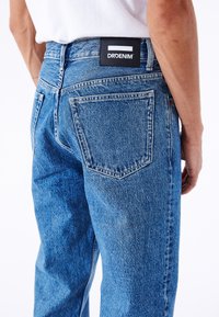 Denim jeans i mellemblå med en løs pasform, fem-lomme design og et sort logo patch på den bageste talje. Let falmet tekstur.